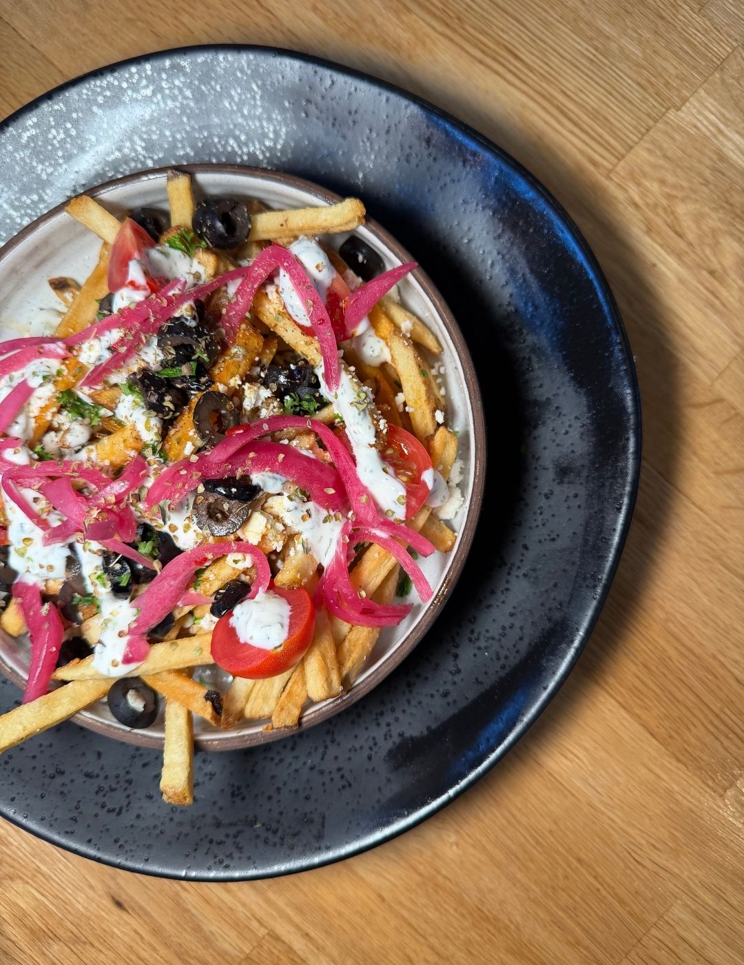 A dark bowl topped with colorful ingredients including pickled vegetables and a drizzle of cream sauce