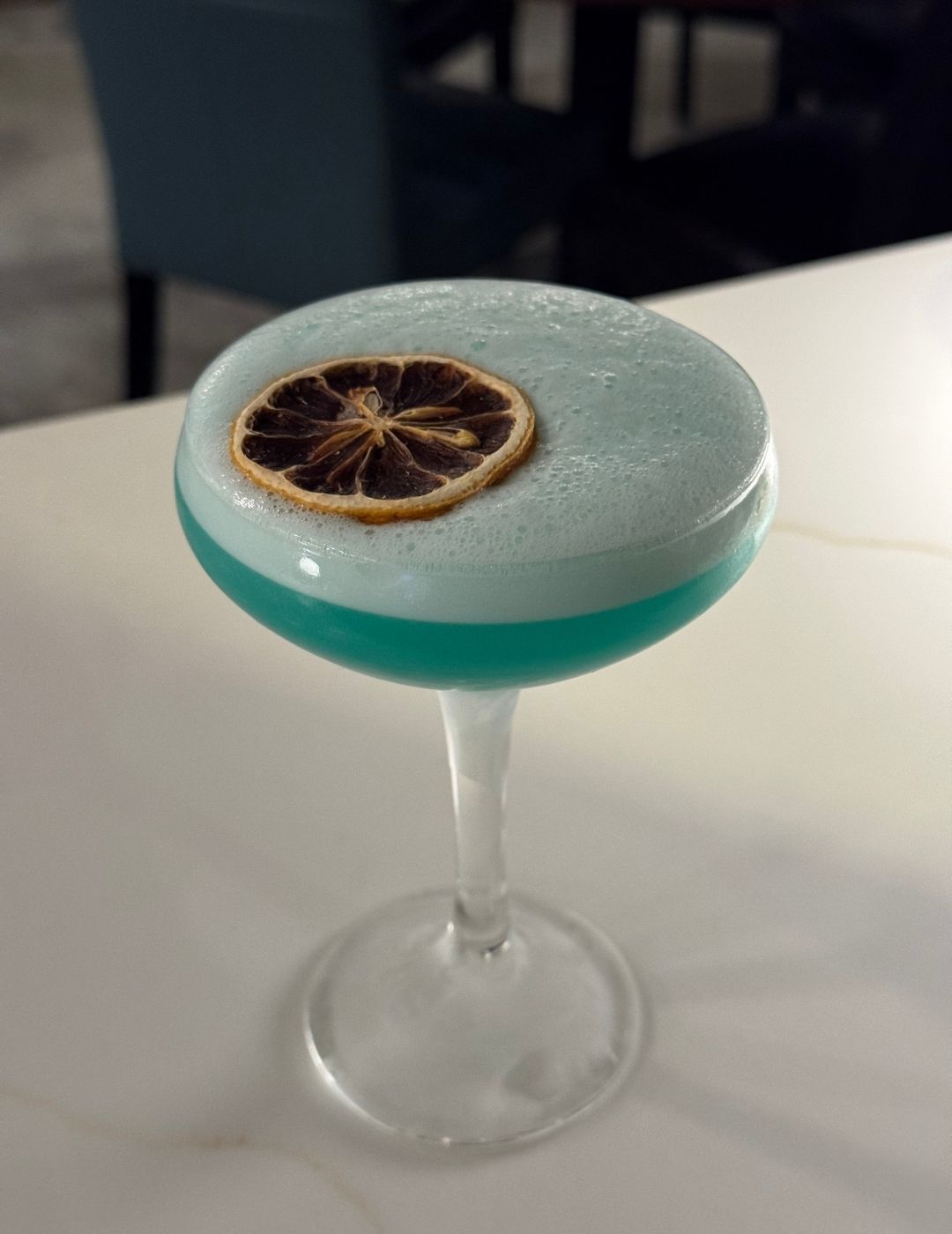 A vibrant blue cocktail garnished with a citrus wheel and decorative pick, served in a coupe glass