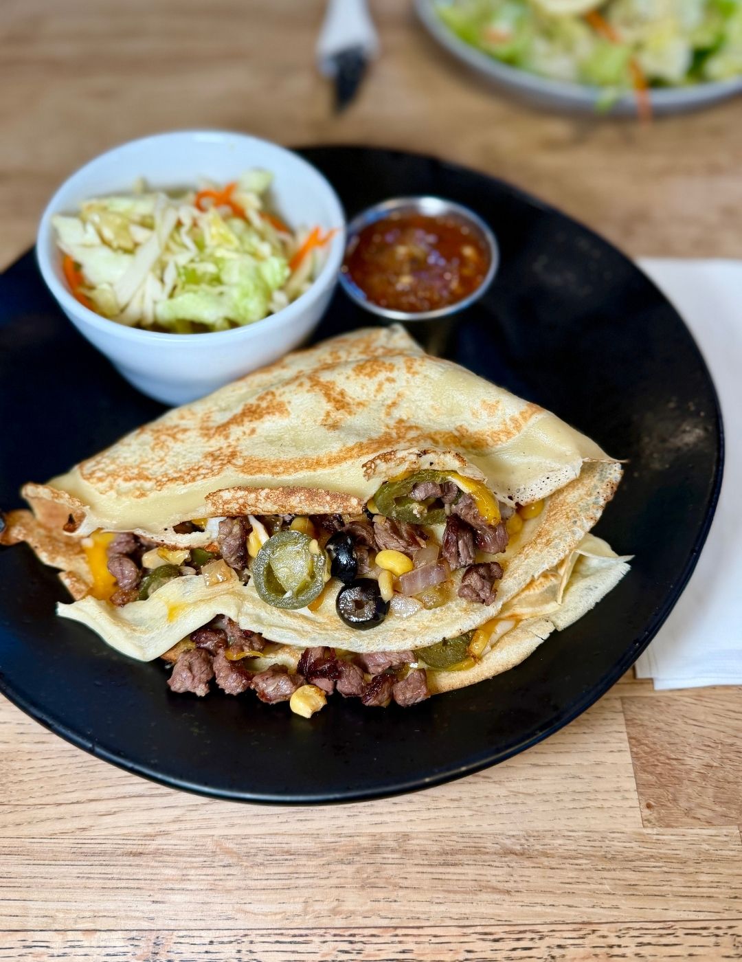 A quesadilla served on a wooden board with dipping sauce