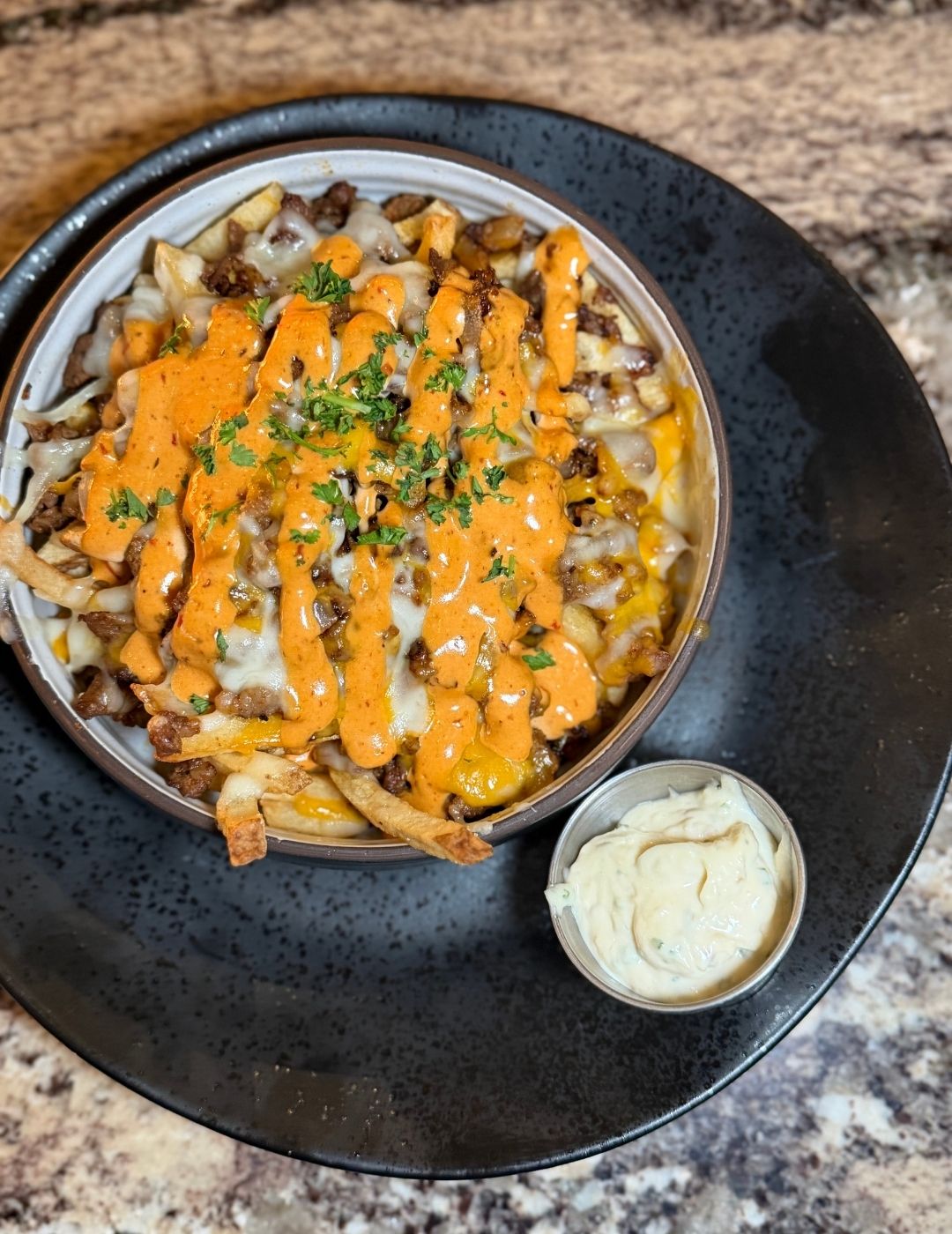 French fries topped with seasoned meat and a creamy white sauce, viewed from above