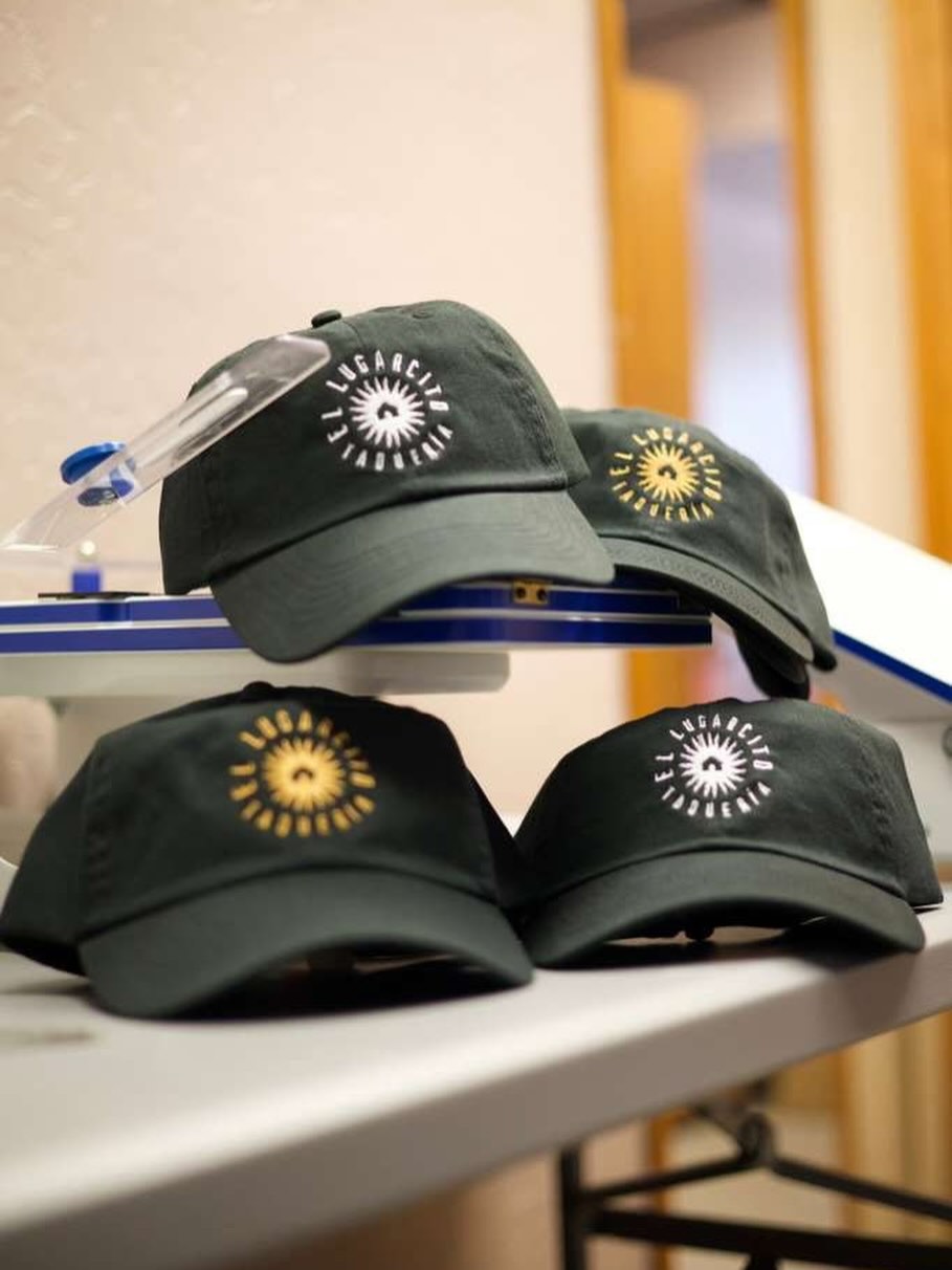 A diverse group of young adults, each wearing a uniquely designed custom shirt or hoodie, standing in a bright studio with creative tools and fabric swatches on a table. The group is smiling and interacting, showcasing individuality and teamwork.