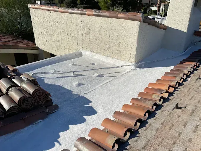 White foam roofing on a flat section beside clay tile roof in Palm Springs, with stucco parapet wall
