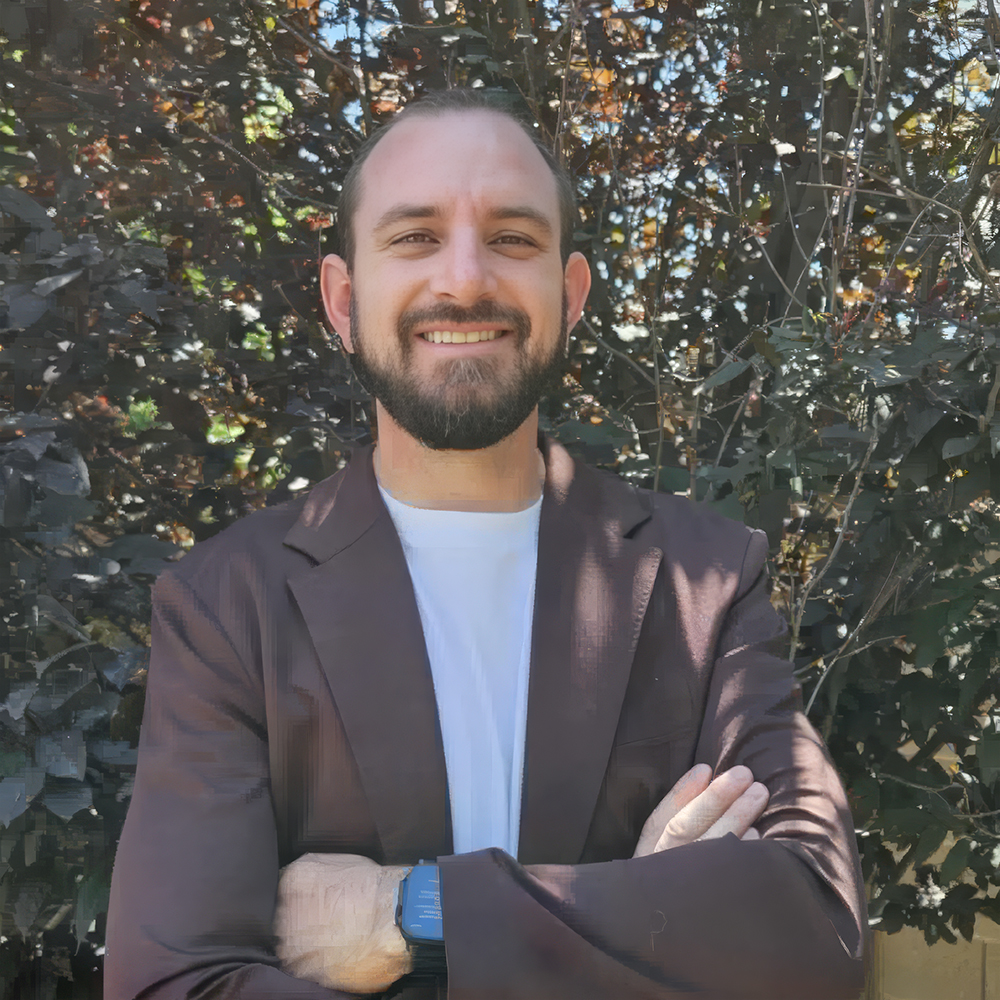 A smiling male AI marketing expert in his 30s, short dark hair, wearing a teal shirt, standing in front of a whiteboard with AI diagrams, modern office, confident and friendly.