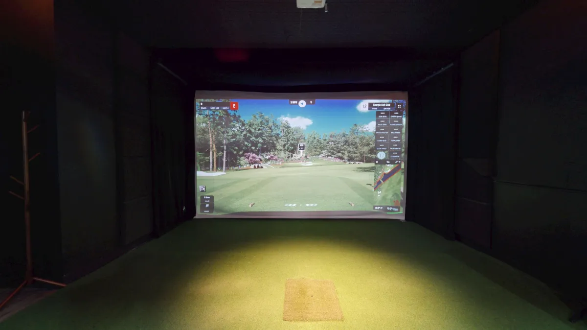 A golf simulator bay with a golf course displayed on the screen.