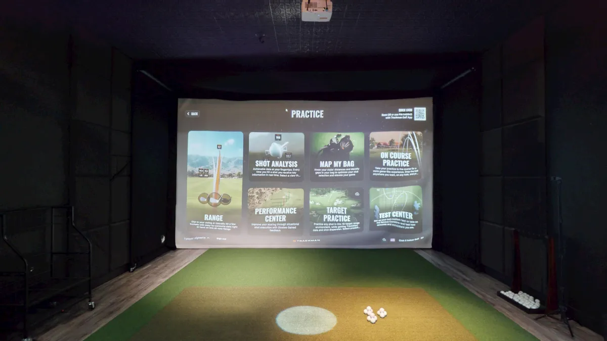 A golf simulator bay with a menu displayed on the screen.