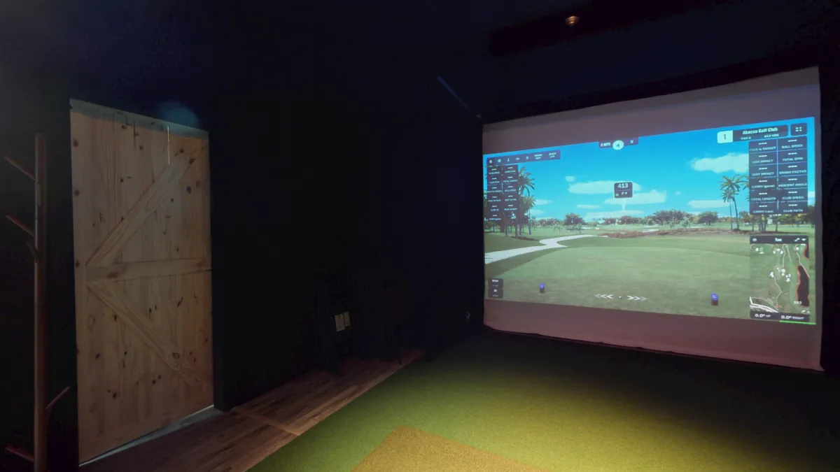 A golf simulator bay with a golf course displayed on the screen.