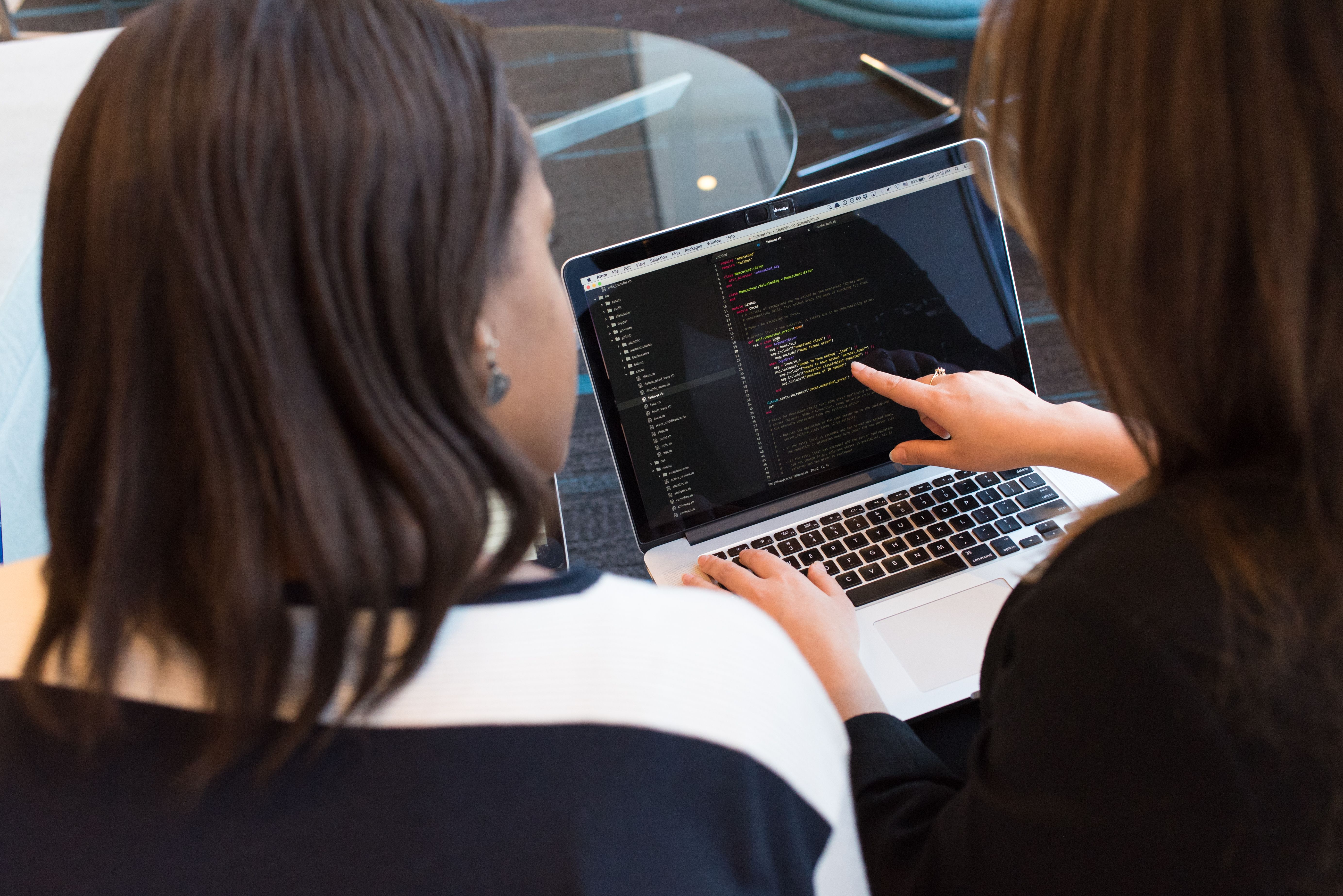 Two women working together on software programming indoors, focusing on coding