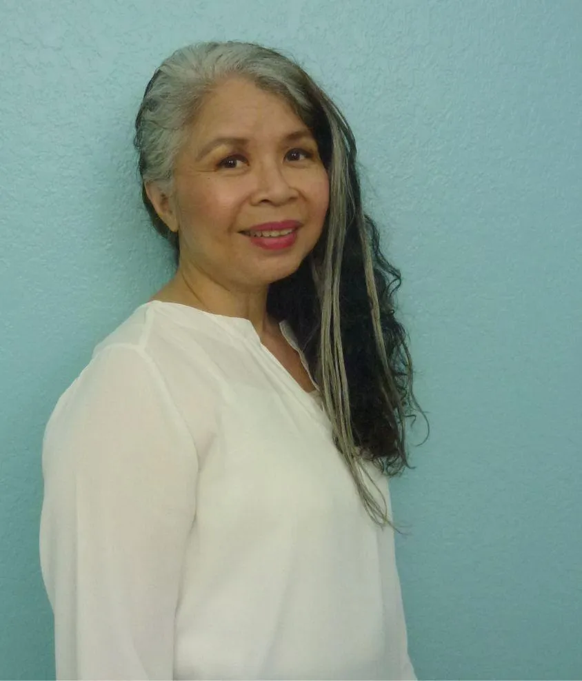 Headshot of a woman in white shirt and aqua background. Salt and pepper hair, smiling