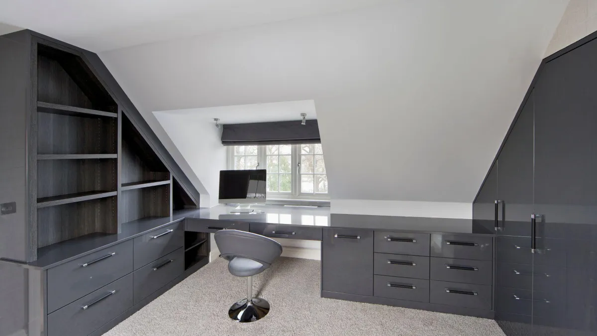 Contemporary attic home office featuring sleek charcoal grey built-in cabinets and desk, a cozy study nook with a large window allowing for natural light, matched with a stylish and comfortable swivel chair on plush carpet flooring, ideal for productive and inspired work from home days.