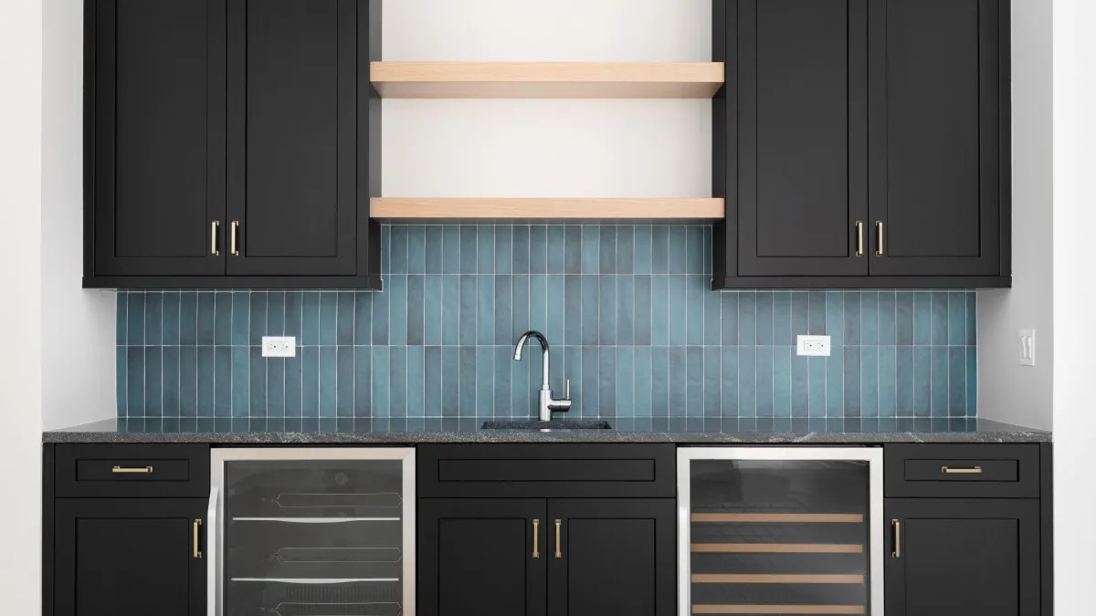 Modern wet bar design featuring elegant dark cabinets, chic blue tile backsplash, and floating wooden shelves, complete with a built-in wine cooler and sophisticated hardware – a stylish addition to upscale interiors.