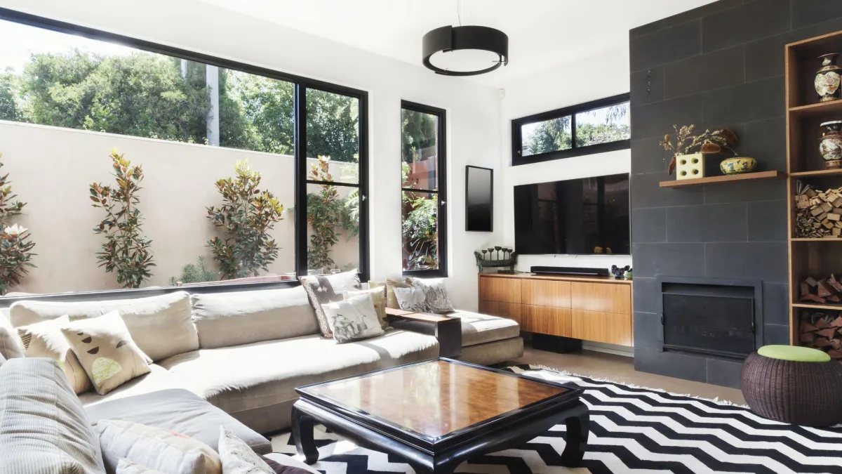 Chic and inviting living room designed for relaxation and entertainment featuring a modern fireplace, built-in shelves for décor, large windows allowing natural light, and a comfortable sectional sofa complemented by a striking black and white patterned rug.