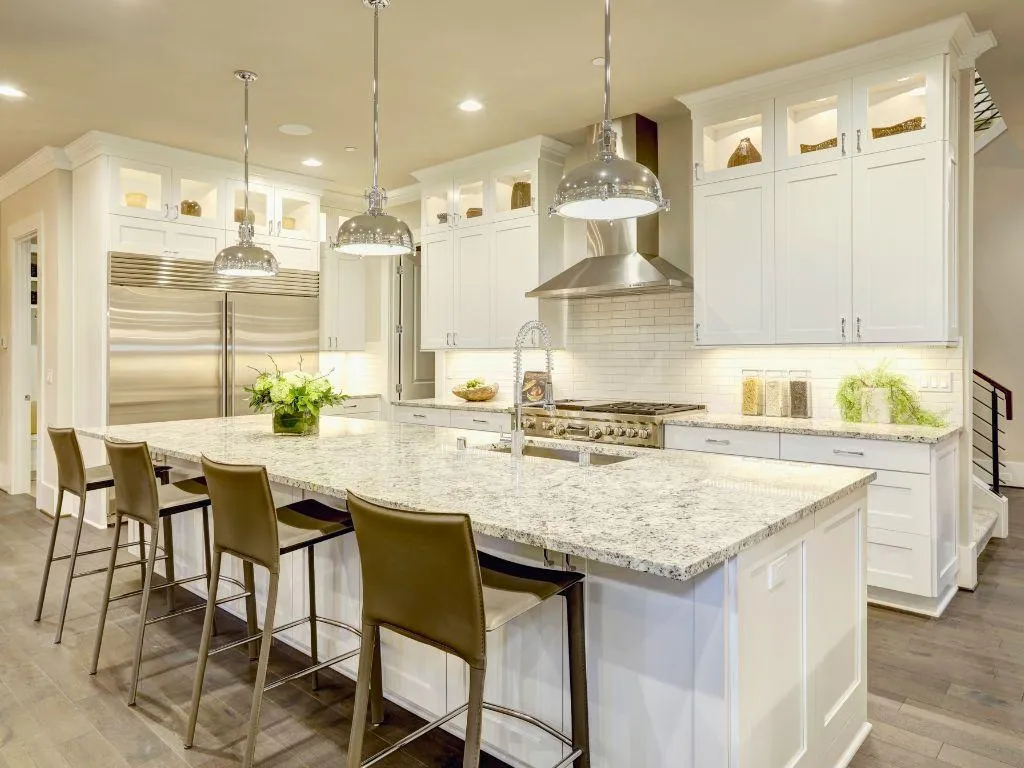 Luxury white kitchen with granite island, stainless steel appliances, and modern pendant lighting by Elci Cabinets and Floors