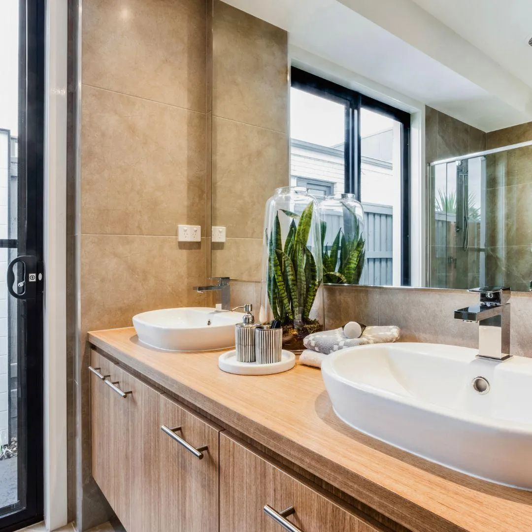 Modern bathroom with natural wood vanity, double sinks, large mirror, and greenery accents by Elci Cabinets and Floors.
