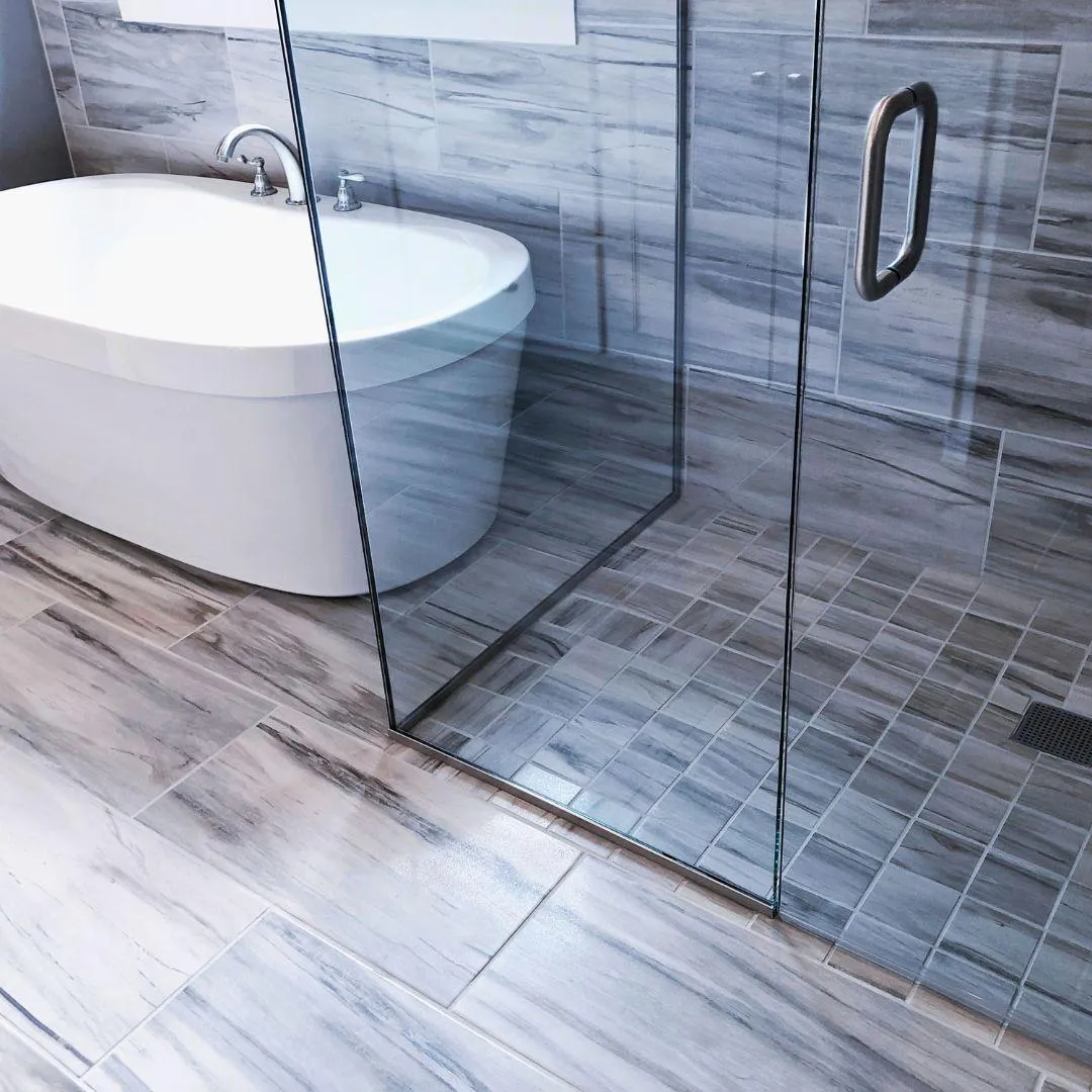 Luxury bathroom with gray marble tile flooring, glass shower enclosure, and freestanding tub by Elci Cabinets and Floors.