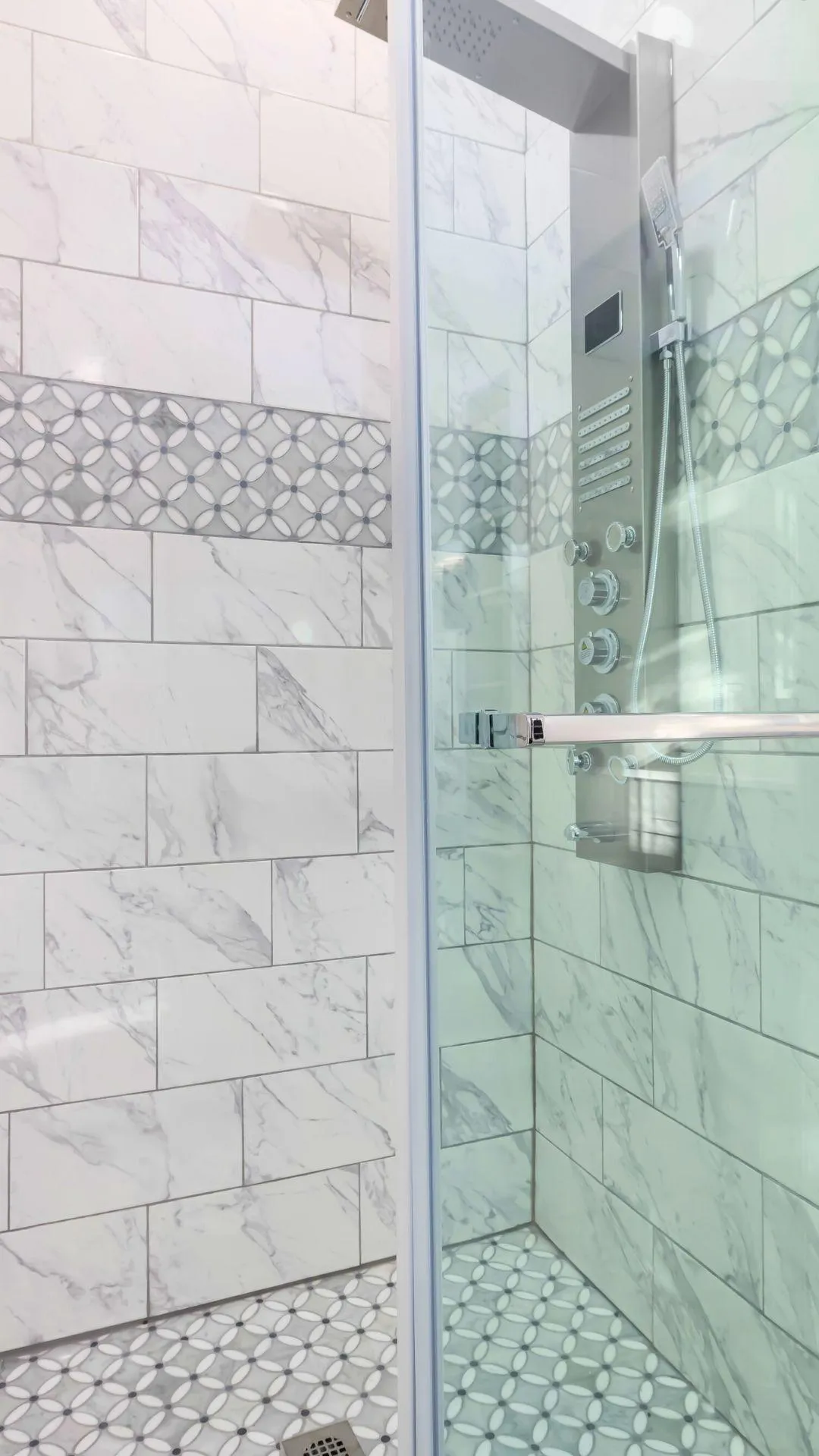 Modern luxury shower with marble walls, decorative accent tiles, and a sleek stainless steel shower panel by Elci Cabinets and Floors.