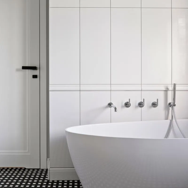 Minimalist bathroom with a sleek freestanding tub, black-and-white patterned flooring, and modern wall-mounted fixtures by Elci Cabinets and Floors.