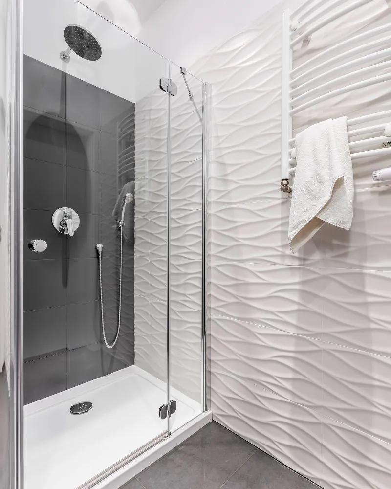 Modern shower with wave-textured white tiles, glass enclosure, and sleek black accent wall by Elci Cabinets and Floors.