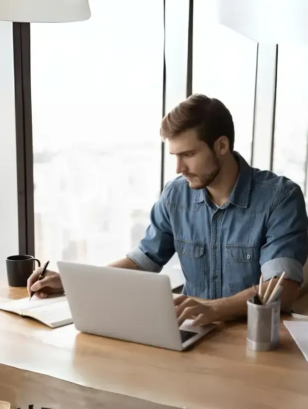 Small business owner taking an online course on a laptop writing notes on a notebook