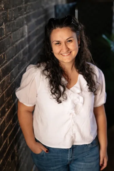 Alex Rice Smiling in a white shirt next to a brick wall.