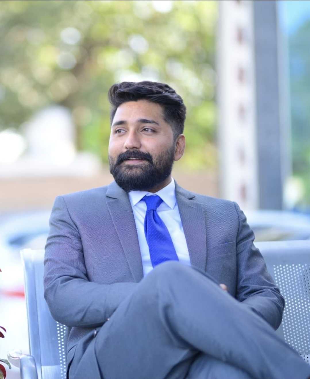Rana Zubair of SKF Practice Solutions wearing a gray suit and blue tie, seated outdoors and looking to the side.
