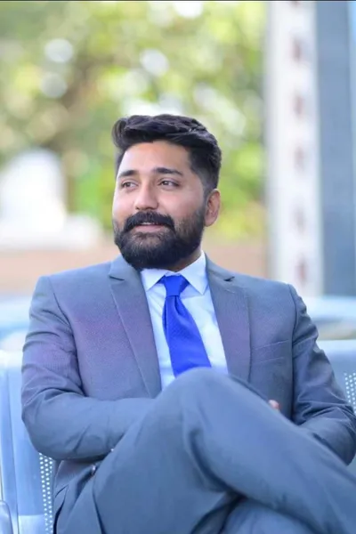 Rana Zubair of SKF Practice Solutions wearing a gray suit and blue tie, seated outdoors and looking to the side.