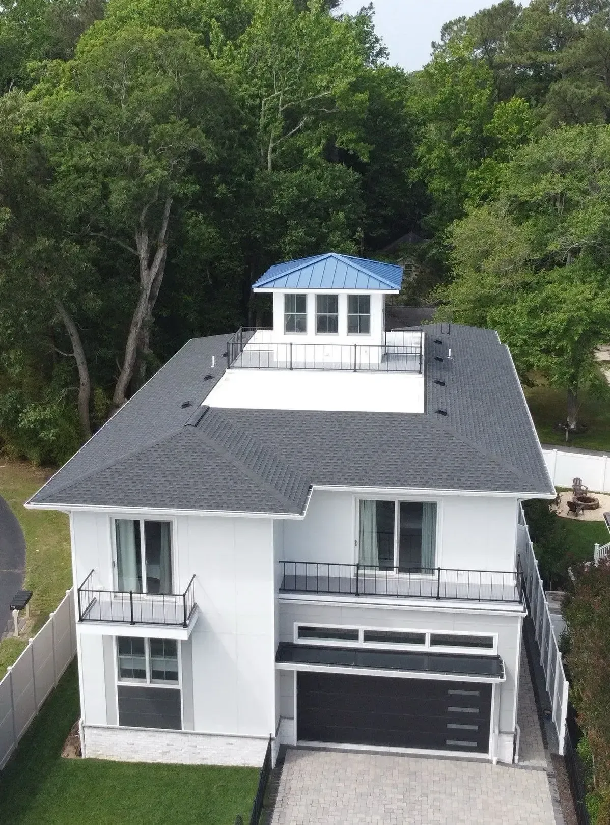 White coastal home with a dark shingle roof, balcony, and rooftop cupola