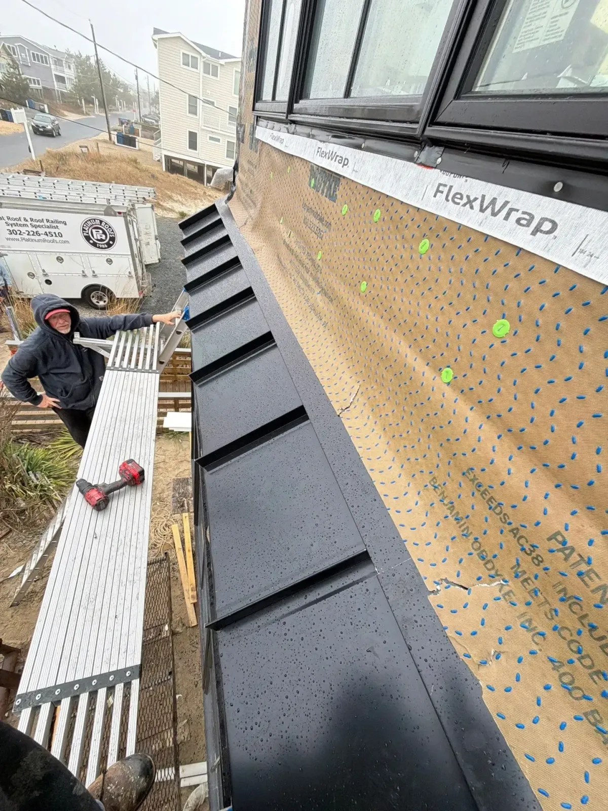 Roofer inspecting metal flashing along a low-slope roof beside exterior windows