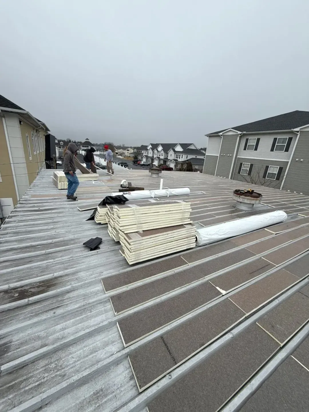 Commercial flat roof replacement with insulation boards, roofing materials, and workers on site