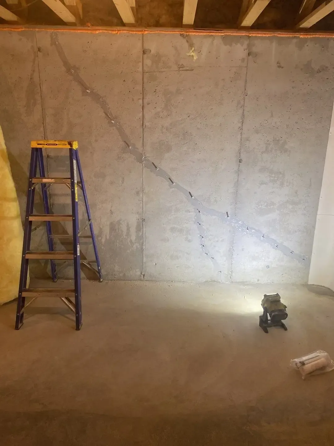Interior concrete foundation wall with a ladder during leak-repair preparation