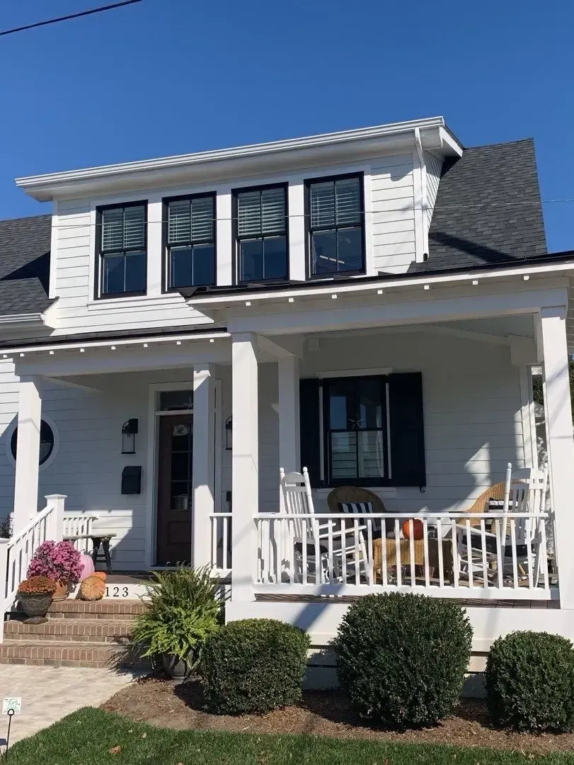 White two-story home with gutters beneath a tree-lined roof edge
