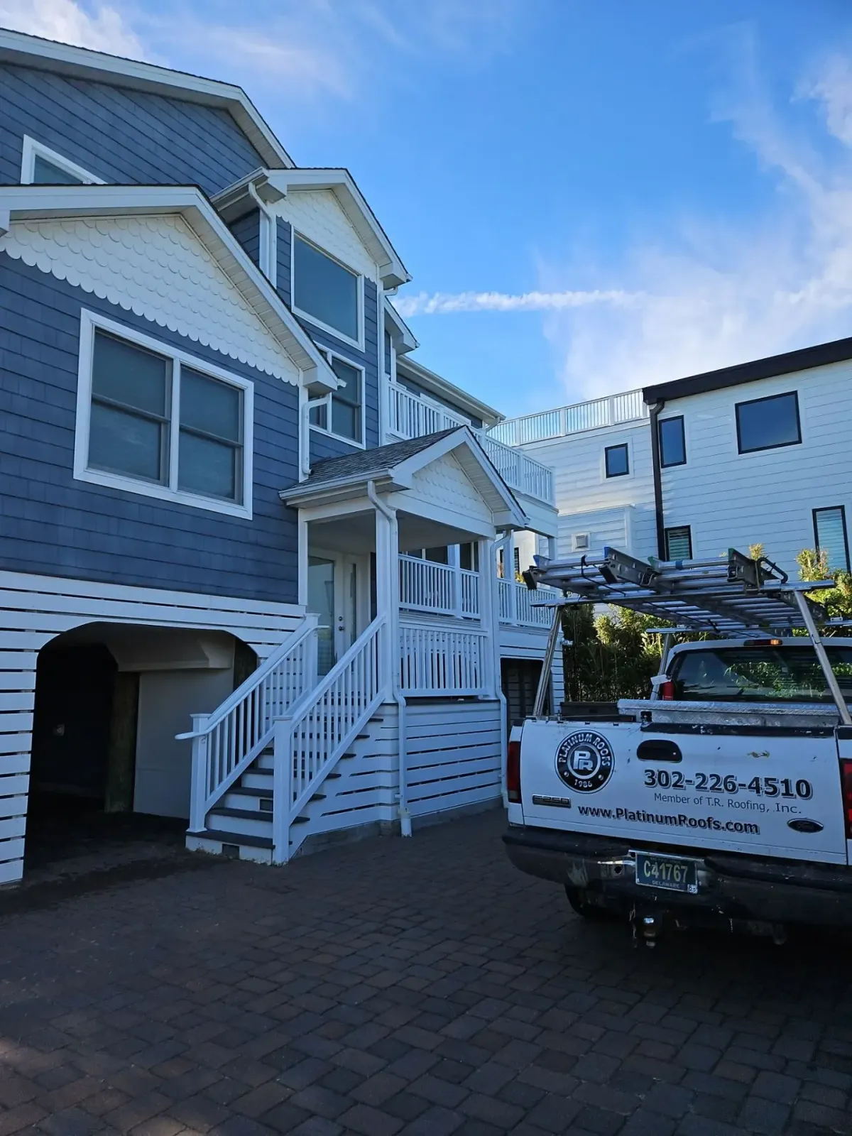 Platinum Roofs service truck beside a blue and white coastal home in Dewey Beach