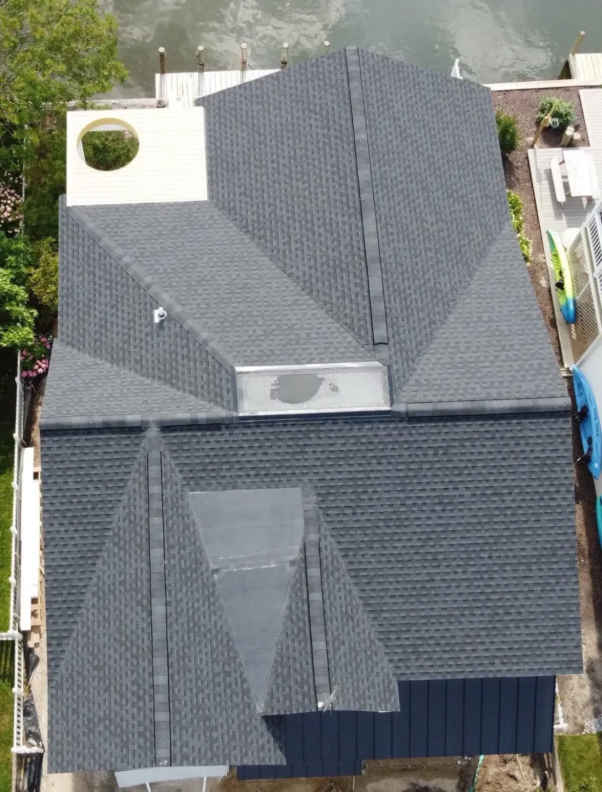 Overhead view of a gray asphalt-shingle roof with multiple hips, valleys, and adjoining low-slope roof sections.