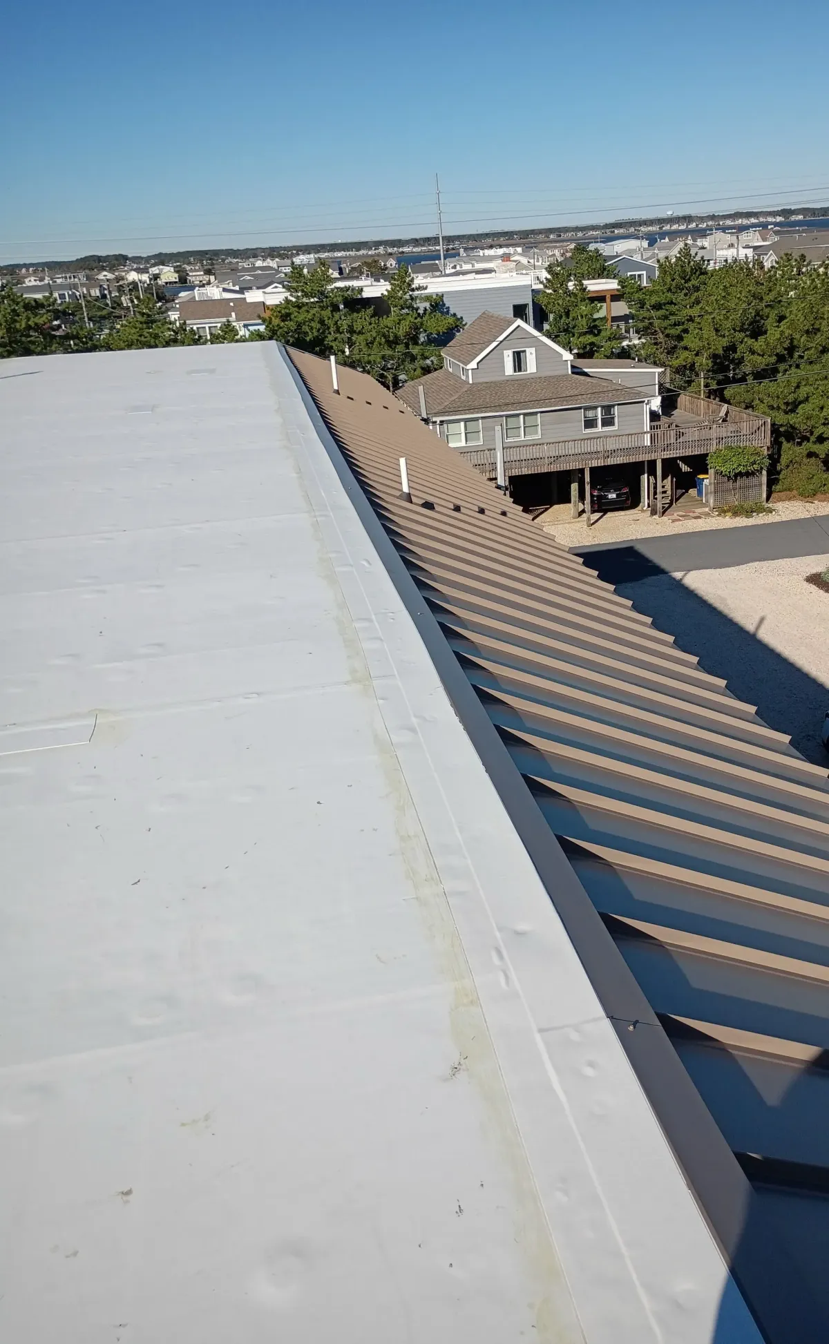 White flat-roof membrane beside brown standing-seam metal roofing at 1301 Bunting Avenue in Fenwick Island, Delaware.