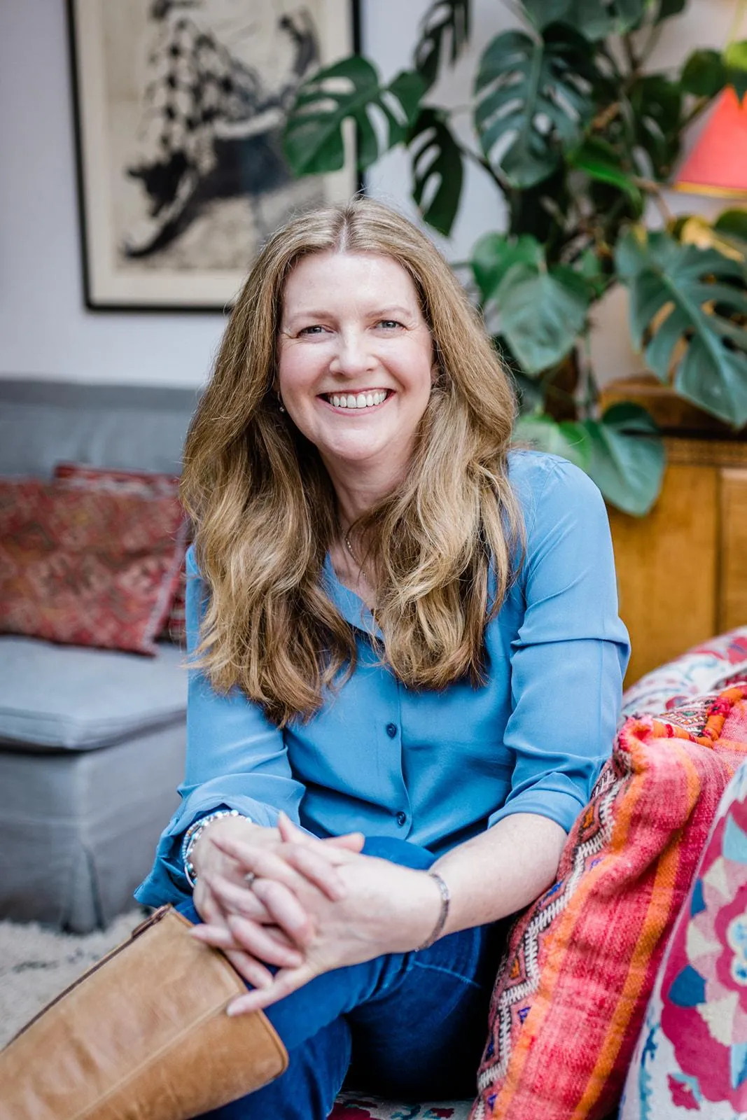 Suzi sitting, smiling on a couch wearing blue jeans, a blue shirt and leather boots.