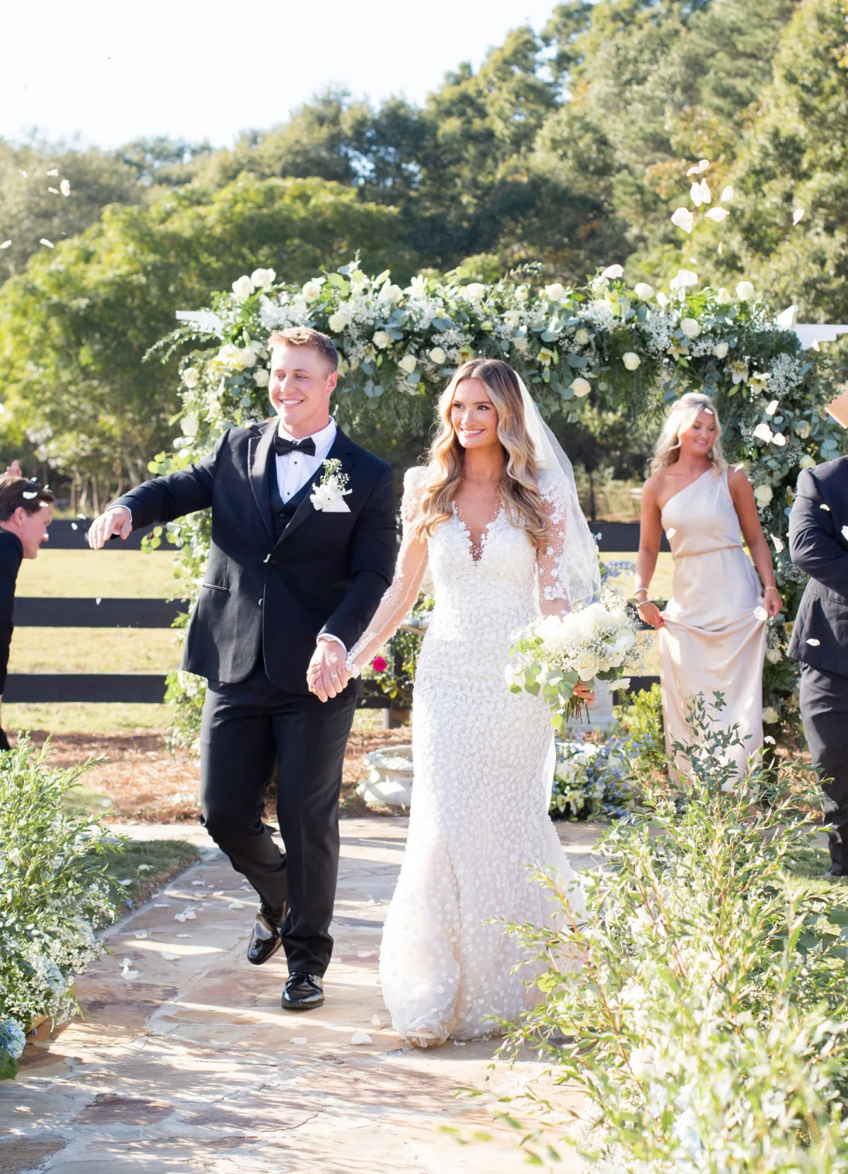 Newlyweds walk back down the aisle after their outdoor ceremony at The Grove Estate while guests toss white petals