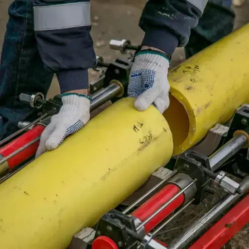 Worker aligning and connecting large yellow sewer pipes using specialized fusion equipment during a pipe replacement project.