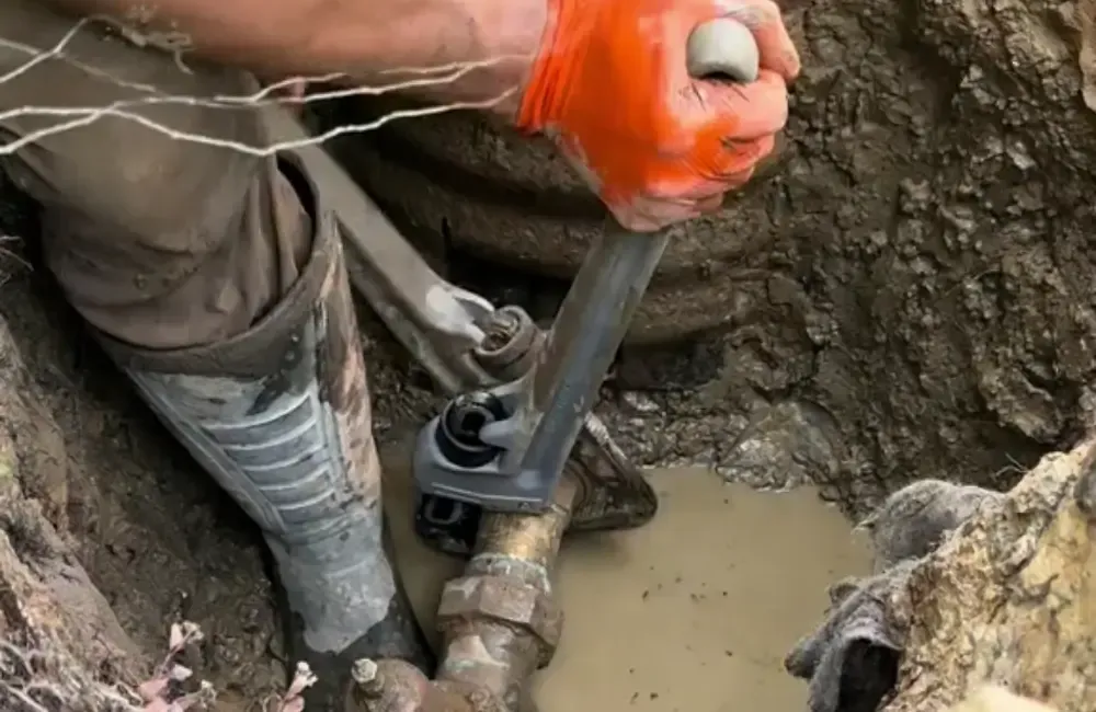 Plumber repairing an underground water line with a pipe wrench