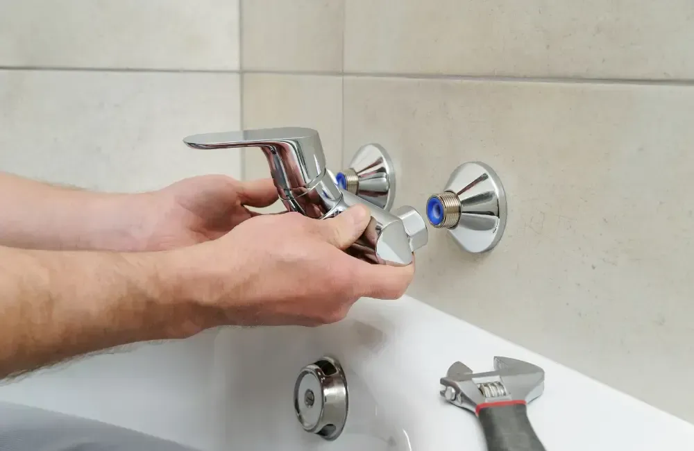 Plumber installing a chrome faucet fixture above a bathtub