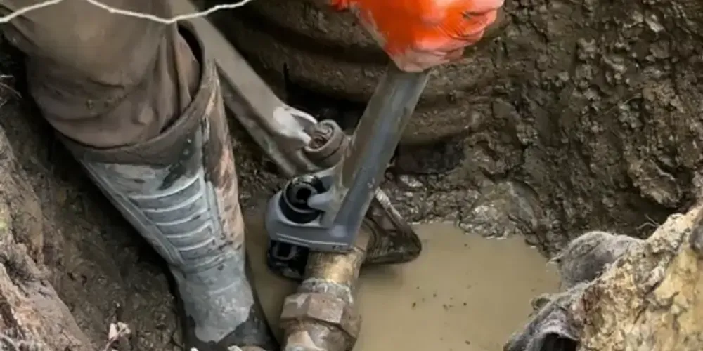 Worker repairing an underground pipe in an excavated trench.