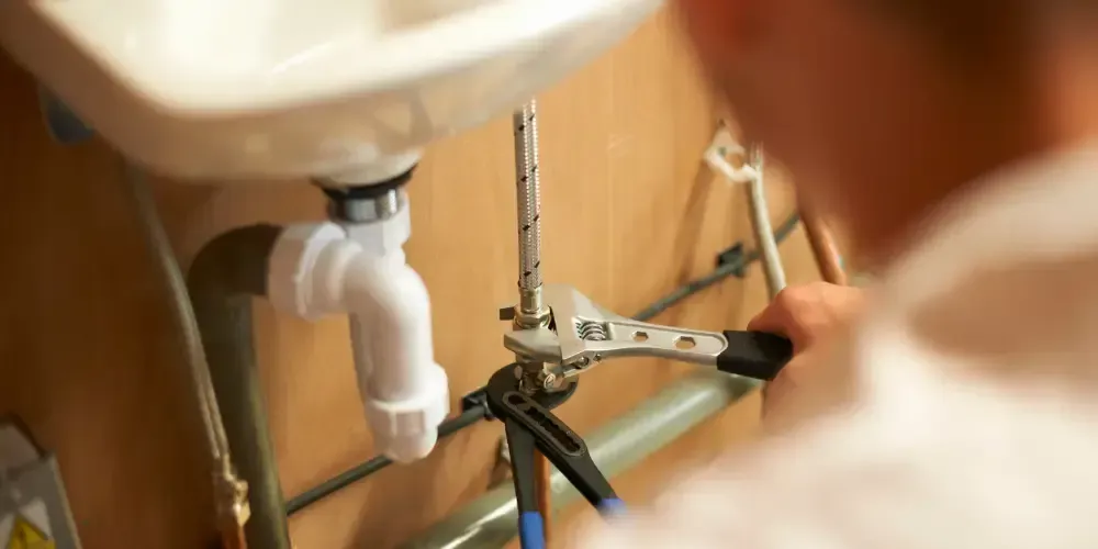 Plumber repairing residential plumbing beneath a sink.