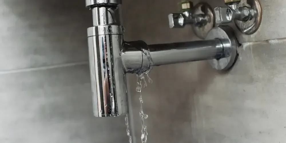 Water leaking from a damaged pipe beneath a sink.