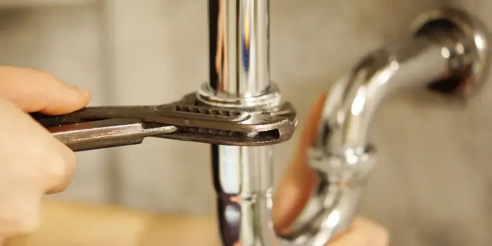 Plumber tightening a chrome drain pipe connection beneath a sink.