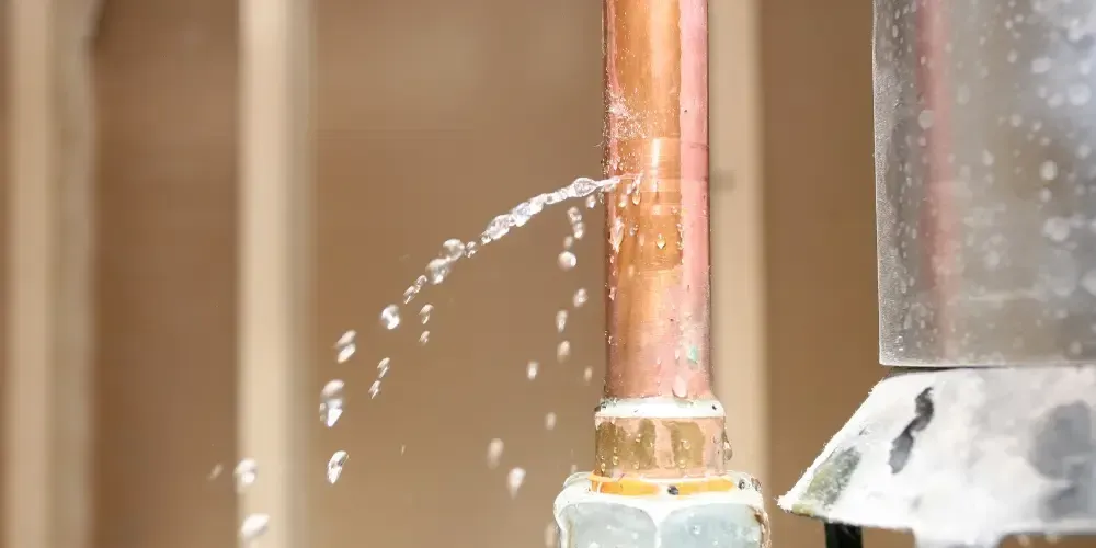 Water spraying from a leak in a copper plumbing pipe.