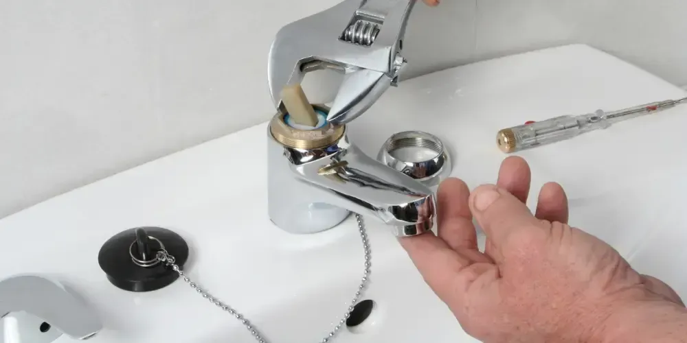 Plumber using an adjustable wrench to repair a sink faucet.