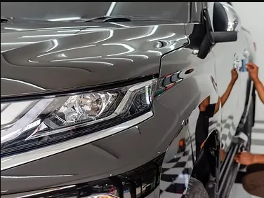 A white yacht docked at a marina, with a detailer polishing the hull under clear blue skies, and an RV parked nearby, both gleaming and surrounded by water and palm trees.