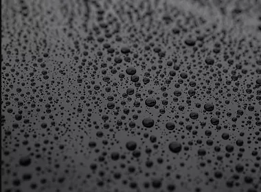 A technician using a dual-action polisher on a deep blue sedan, with dramatic before-and-after reflections visible on the hood, set in a well-lit, professional detailing bay.