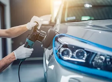 A white yacht docked at a marina, with a detailer polishing the hull under clear blue skies, and an RV parked nearby, both gleaming and surrounded by water and palm trees.