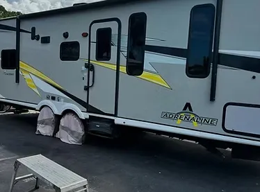 A luxury SUV being detailed in a residential driveway, with a technician using a high-pressure washer, surrounded by lush greenery and sunlight, emphasizing convenience and premium service at home.