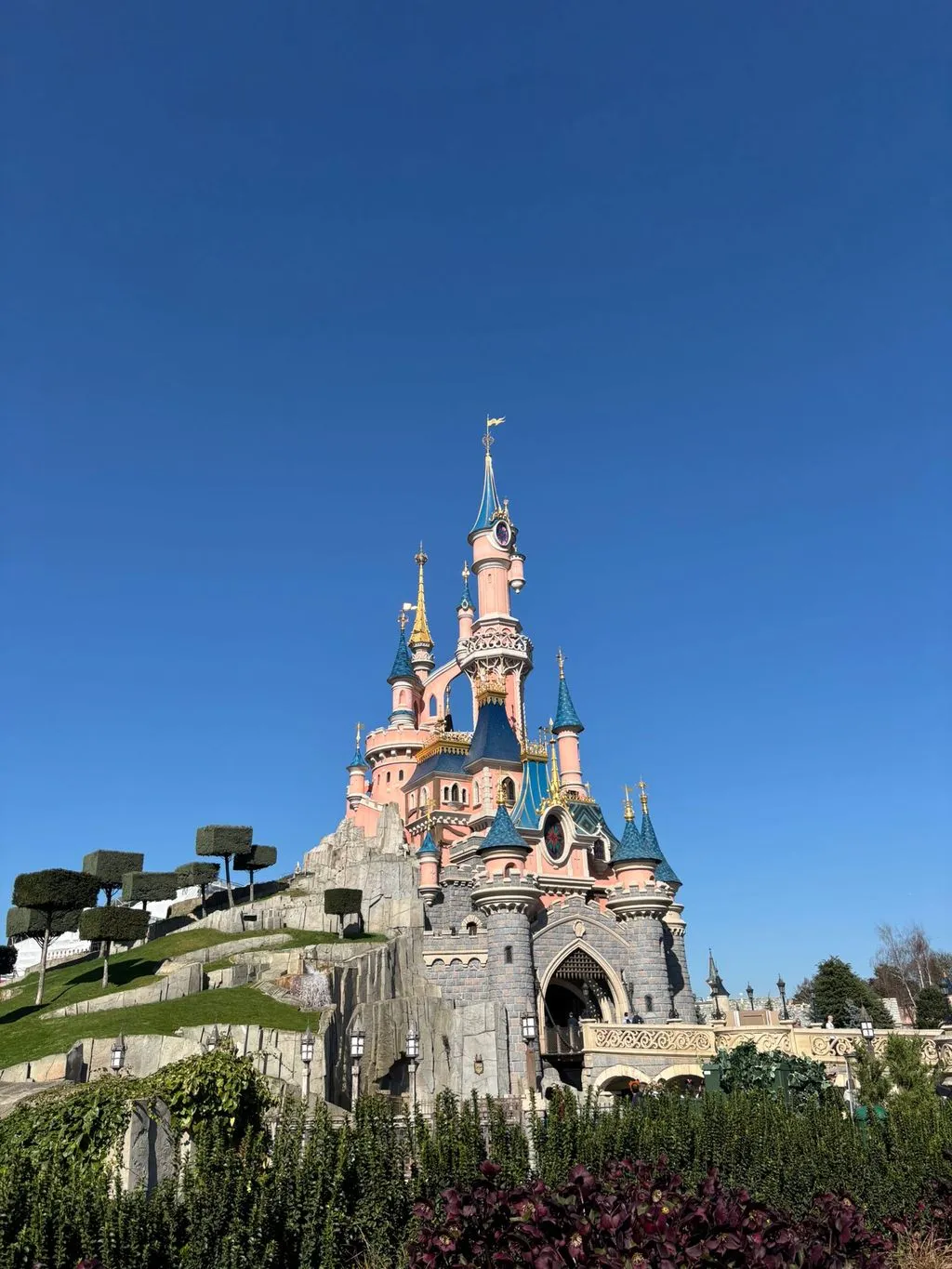 the pretty pink disneyland paris castle sits against a bright blue sky