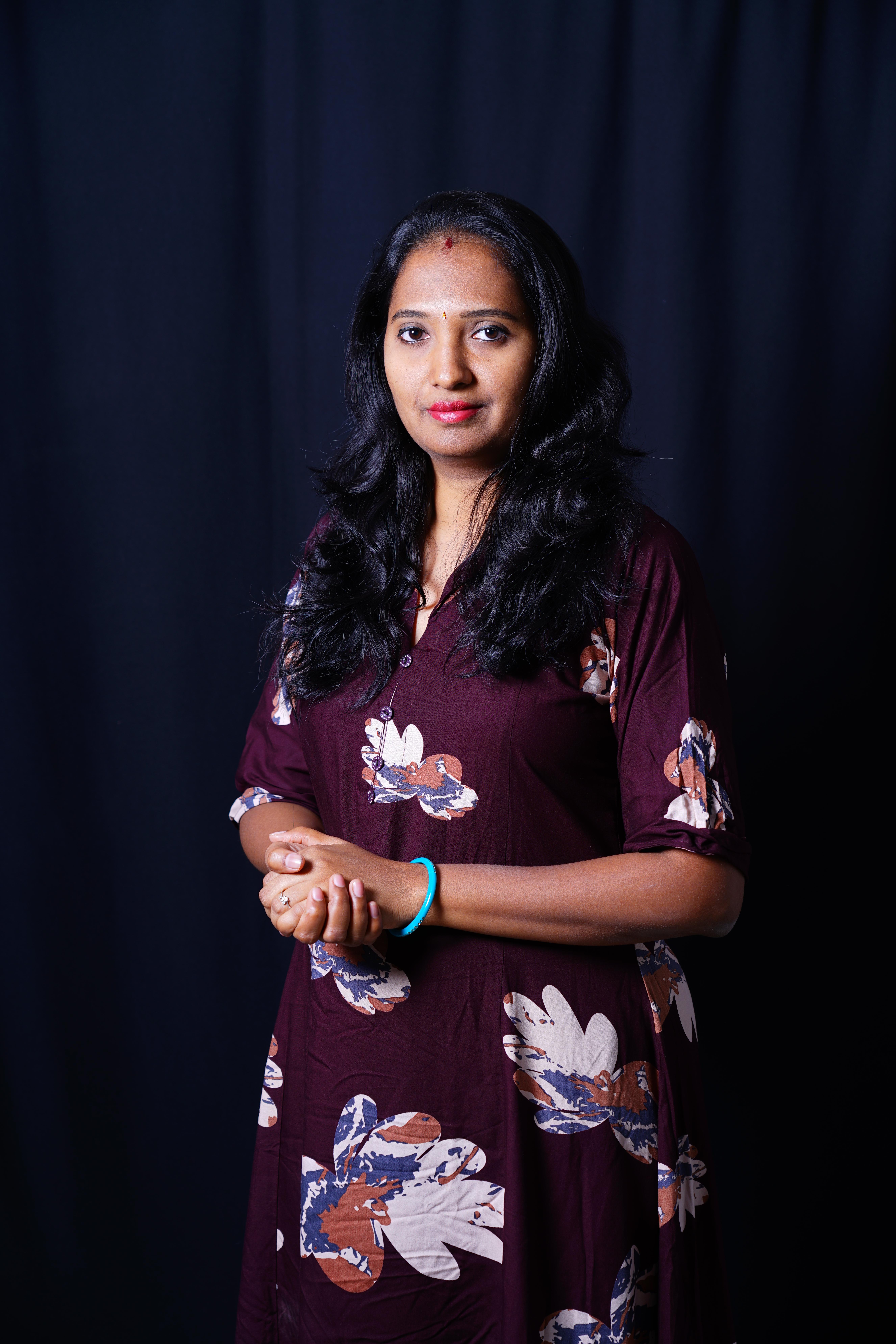 A professional portrait of a Tamil woman in her 40s, wearing a smart saree, smiling confidently against a soft, neutral background, exuding warmth, expertise, and approachability.